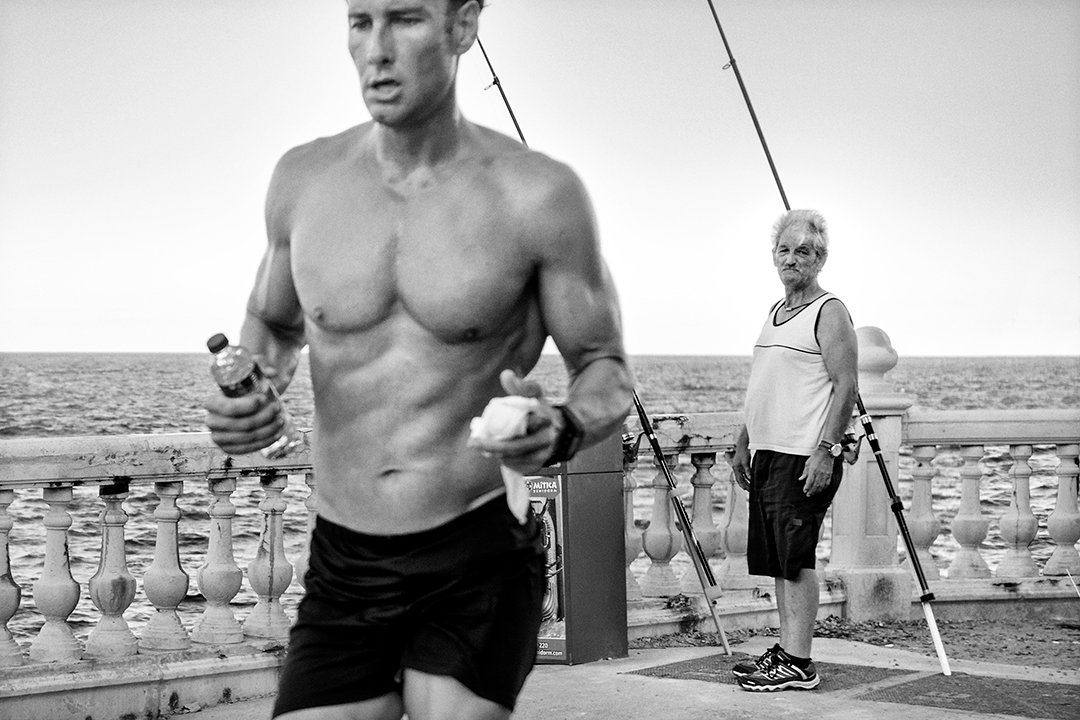 A man runs beside a balustrade overlooking the sea.